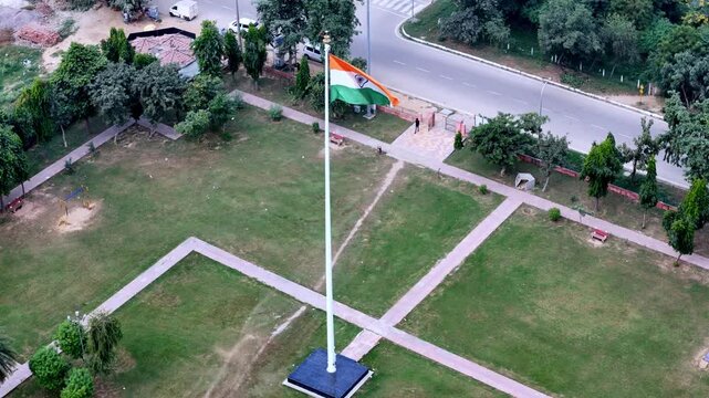 Aerial view of the Indian flag flying on a tall pole in a public park with green lawns and paved walkways in Greater Noida, Uttar Pradesh, India.