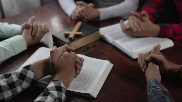 Group of people praying together around a wooden table in a room, sharing faith, hope, peace, love, and spiritual support.