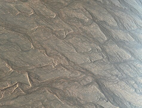 Intricate wet sand patterns shaped by retreating seawater. Natural textures with delicate silver and golden tones create an abstract coastal background with a subtle metallic sheen.