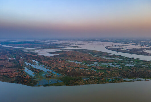 Aerial view of Qadirabad Head Works Bridge spanning the Chenab River, surrounded by marshy wetlands and lush vegetation under a soft twilight sky in Wazirabad, Punjab, Pakistan.