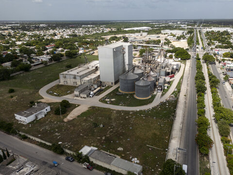 Aerial view of a corn flour factory featuring large metal silos and industrial buildings surrounded by green space near a road in Merida, Yucatan, Mexico.