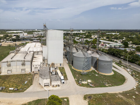 Aerial view of a corn flour factory with large metal silos and industrial buildings surrounded by green fields and trees in Merida, Yucatan, Mexico.