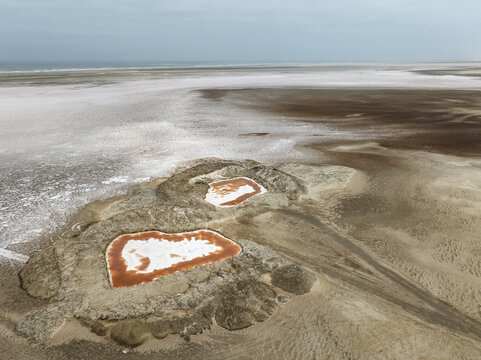 Aerial view of the Skeleton Coast salt pans with distinctive reddish pools and white salt crusts stretching towards the Atlantic Ocean, Dorob National Park, Kunene Region, Namibia.