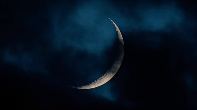 Moon crescent with clouds rolling by in the night sky. Astrophotography real footage of the lunar view.