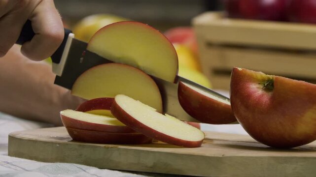 Closeup, slow motion shot of sharp knife slicing up apple on cutting board