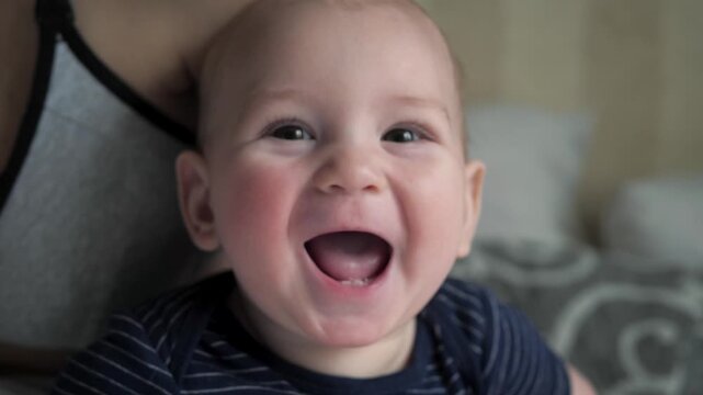 Portrait of cute infant boy with rosy cheeks looking at camera and starting to laugh. The baby's face lights up with a joyful and genuine smile, expressing pure happiness