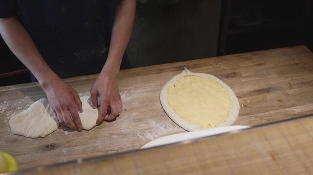 Close-up of a master working with pizza or khachapuri dough. Manually forming the base and sides on a wooden work surface.