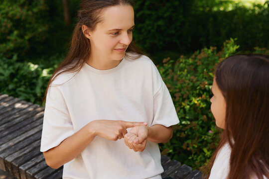 Two individuals converse using sign language in a garden filled with plants. They sit on a stone bench surrounded by greenery during the day
