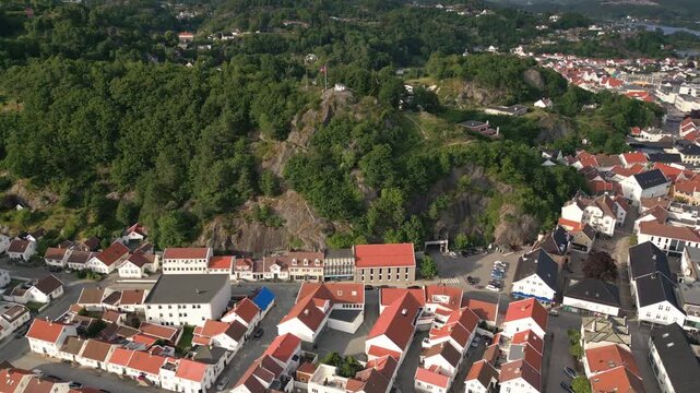 Aerial view of the coastal town of Mandal featuring traditional white wooden houses, red roofs, and a lush green hill in Mandal, Agder, Norway.