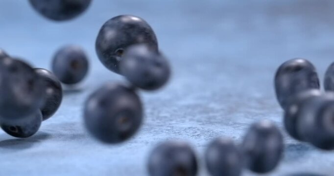 Fresh blueberries fall and bounce across a blue surface in slow motion