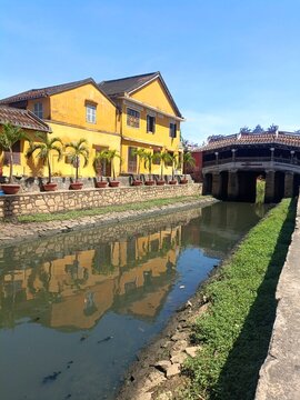 Japanese Covered Bridge and yellow buildings reflected in canal water at Hoi An, Vietnam