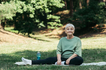 Obraz premium Smiling senior woman enjoys exercising in a beautiful green park