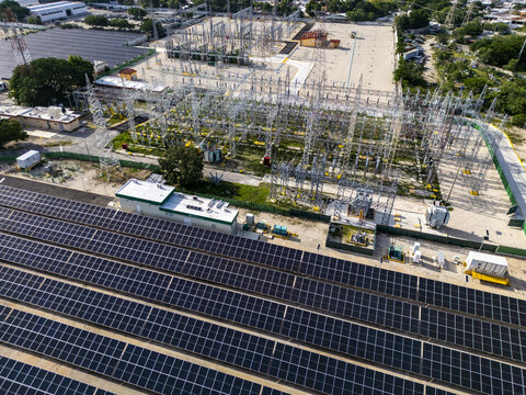 Aerial view of a solar farm with rows of photovoltaic panels and an electrical substation featuring metal structures and transformers in Merida, Yucatan, Mexico.
