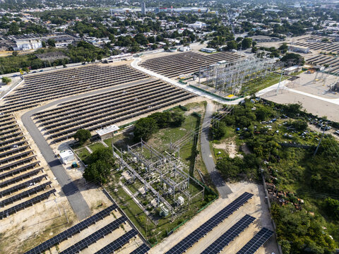 Aerial view of a large solar farm with rows of photovoltaic panels and an electrical substation situated in the urban landscape of Merida, Yucatan, Mexico.