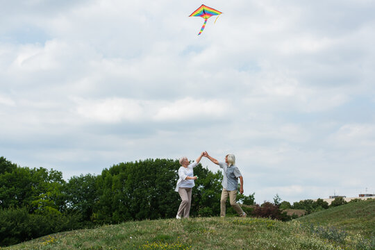 Joyful seniors flying a colorful kite together in a sunny meadow