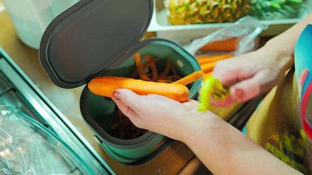 Woman peels a fresh carrot while placing the peels into household bio waste bin