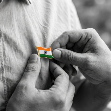 Meaningful India Independence Day patriotic close up of hands attaching an Indian tricolor flag pin to clothing with selective color, symbolizing unity, respect, freedom, honor and national pride