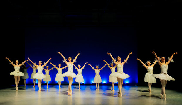 Ballet dancers perform a choreographed routine in white tutus on stage