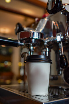 Close-up of espresso machine preparing coffee into takeaway paper cup in warm cafe lighting. Shallow depth of field, cozy atmosphere, modern coffee culture concept