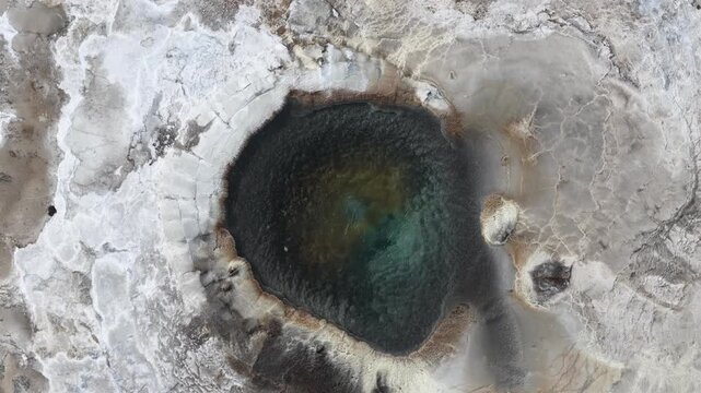 Aerial view of geothermal pool with vibrant blue water surrounded by mineral-rich crusty terrain in Hveravellir, Hrunamannahreppur, Iceland.