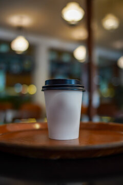 Minimal coffee cup on wooden table with warm bokeh lights in cafe. Clean composition with copy space, cozy lifestyle concept, perfect for branding and advertising.