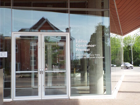 Gatineau,Quebec, Canada &ndash; June 7, 2026: Modern glass doors of "&Eacute;difice Constance-Provost" feature French signage for Biblioth&egrave;que Lucy-Faris and Centre de services d'Aylmer at 115 rue Principale.