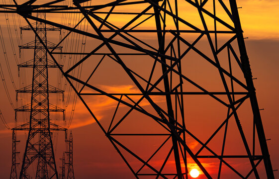 Silhouette of high voltage electricity transmission towers and power lines against a glowing sunset sky. Electrical infrastructure, utility network, energy supply, sustainable engineering, smart grid.