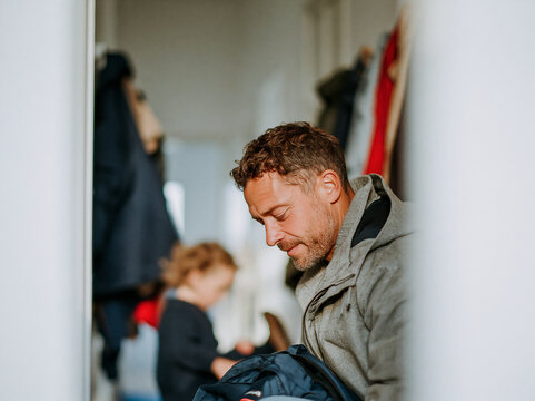Smiling father helping his young child get ready in the hallway at home, authentic involved fatherhood and everyday family moment.