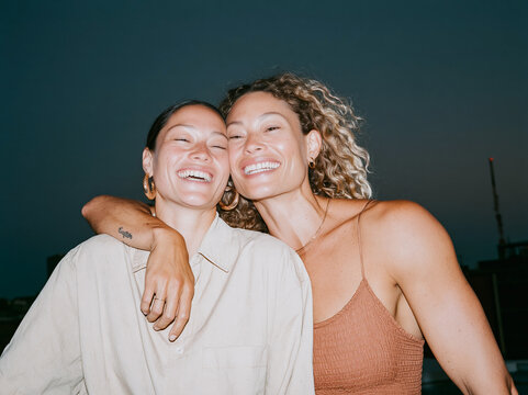 Candid flash snapshot of two happy young women embracing and laughing outdoors at night, authentic friendship moment with retro party aesthetic.