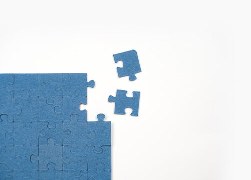 Single blue jigsaw pieces sit separated from a partially assembled puzzle on a clean white surface to represent the final steps of solving a challenging task or completing a logical work goal