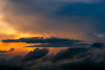 Fototapeta premium Dramatic cumulonimbus storm clouds illuminated by golden sunset light above dark rain clouds creating an extreme weather sky, atmospheric landscape and climate change background with copy space.