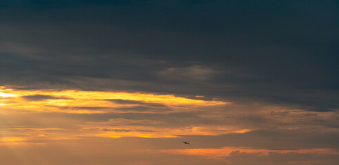 Fototapeta premium Commercial airplane flying beneath dramatic sunset clouds with expansive copy space, symbolizing air travel, aviation, tourism, freedom, business transportation and memorable journey at golden hour.