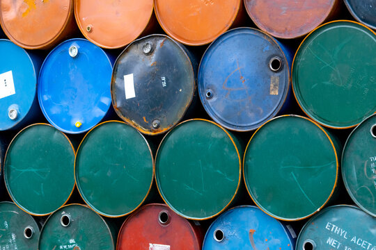 Stacked steel oil and chemical barrels in an industrial warehouse. Hazardous material storage, petrochemical logistics, toxic waste management, factory operations and industrial background texture.