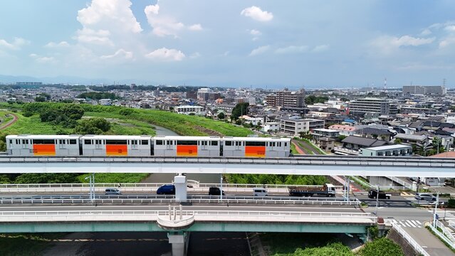 Aerial view of the Tama Monorail crossing the Asakawa River with lush green banks and urban residential buildings in Hino, Tokyo, Japan.