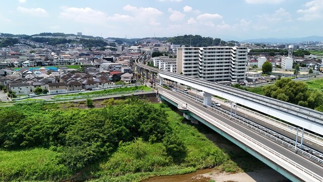 Aerial view of the Asakawa river with a monorail track crossing the bridge, surrounded by residential buildings and lush greenery in Hino, Tokyo, Japan.