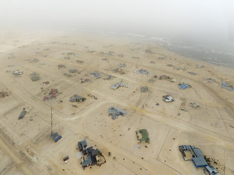 Aerial view of scattered houses in the coastal desert settlement with sandy roads and the Atlantic Ocean in the background under a hazy sky in Wlotzkasbaken, Erongo Region, Namibia.