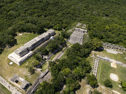 Aerial view of the ancient Mayan ruins of Uxmal, featuring the Pyramid of the Magician and the Nunnery Quadrangle surrounded by lush green jungle in Uxmal, Yucatan, Mexico.