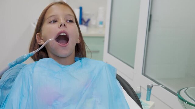 Pediatric dentist inserting saliva ejector for young girl during treatment.