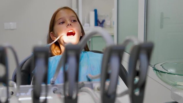 Pediatric dentist inserting saliva ejector for young girl during treatment.
