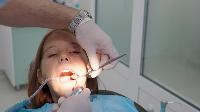 Pediatric dentist examining teeth with mirror for young girl close up.