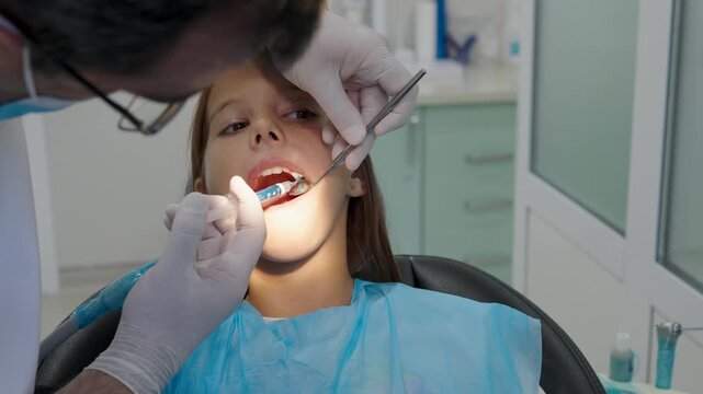 Pediatric dentist giving local anesthesia injection to young girl patient.