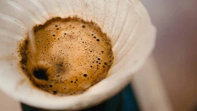 Pour over coffee brewing top view, drip filter coffee blooming with bubbles macro shot, water pouring over ground coffee, specialty coffee extraction process