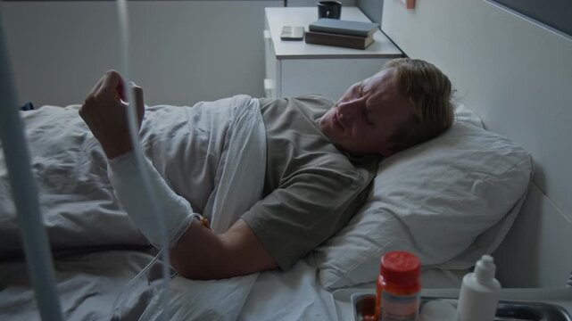 Caucasian man lying in hospital bed with bandaged arm looking at injury and clenching fist. Video for medical insurance, healthcare services, or patient recovery campaigns