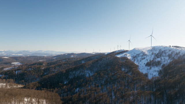 Wind turbines on a snow-covered mountain ridge under a clear blue sky