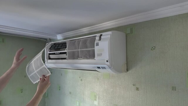 Technician replacing dusty mesh filter in wall mounted air conditioner unit for home maintenance