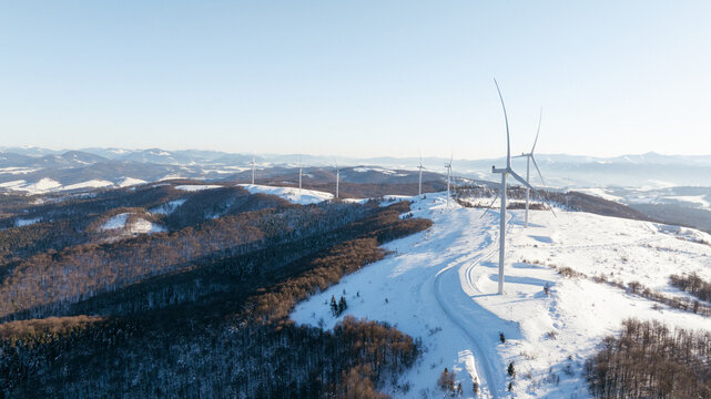 Wind turbines stand tall on a snow-covered mountain range under a clear sky