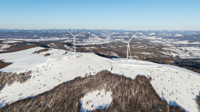 Wind turbines stand tall on a snow-covered mountain landscape under a clear sky