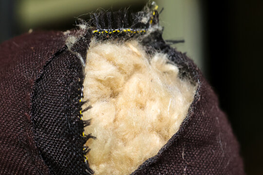 Worn fabric seam with exposed soft stuffing visible through torn upholstery, close up detail showing texture and fibers, slightly frayed edges and repair need