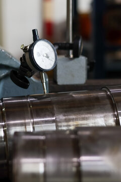 Dial indicator measuring metal shaft tolerance in workshop.