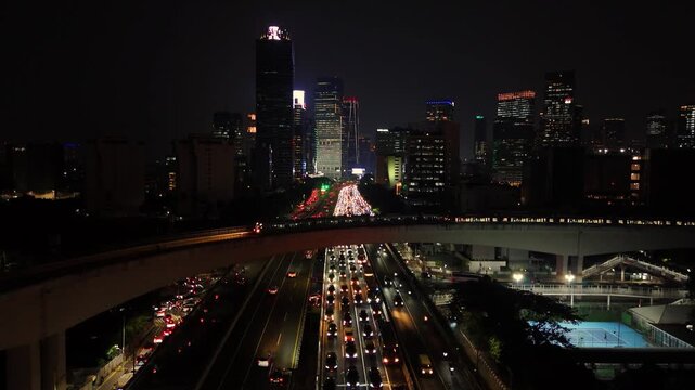 Jakarta, Indonesia - 23 July 2026: Aerial view of the illuminated city skyline at night with heavy traffic flowing along the highway and glowing skyscrapers.